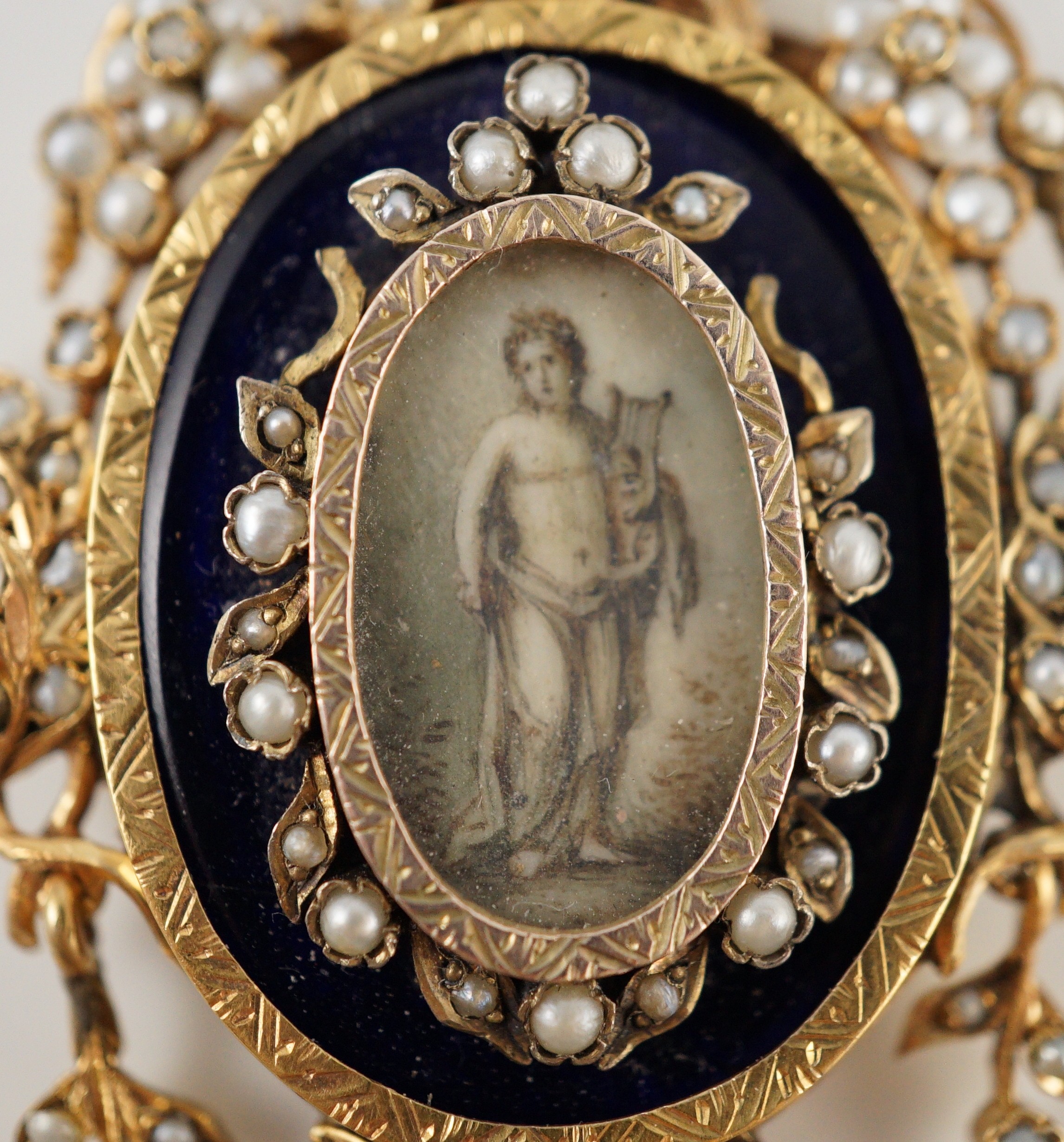 A Regency parcel gilt silver seed pearl and enamel set oval pendant, with inset ivory panel of a semi-clad figure with a lyre
